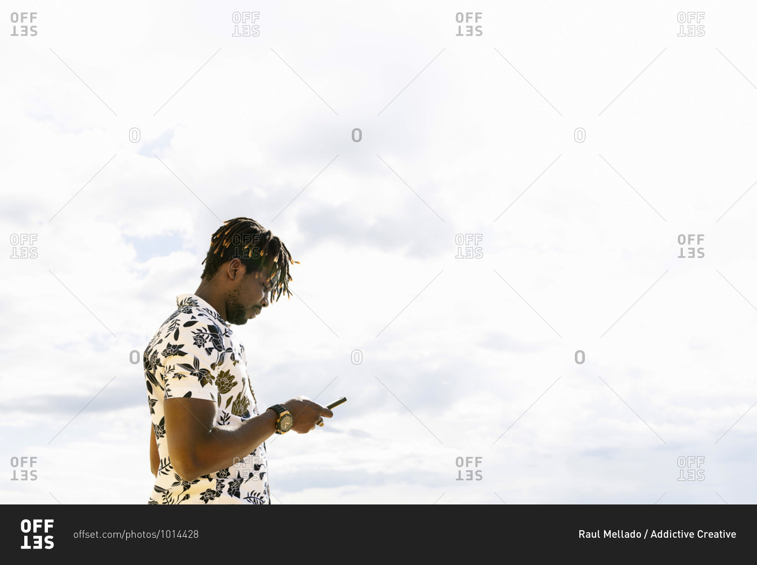 Stylish young black man looking at his mobile phone with the sky in the background, technology and lifestyle concept
