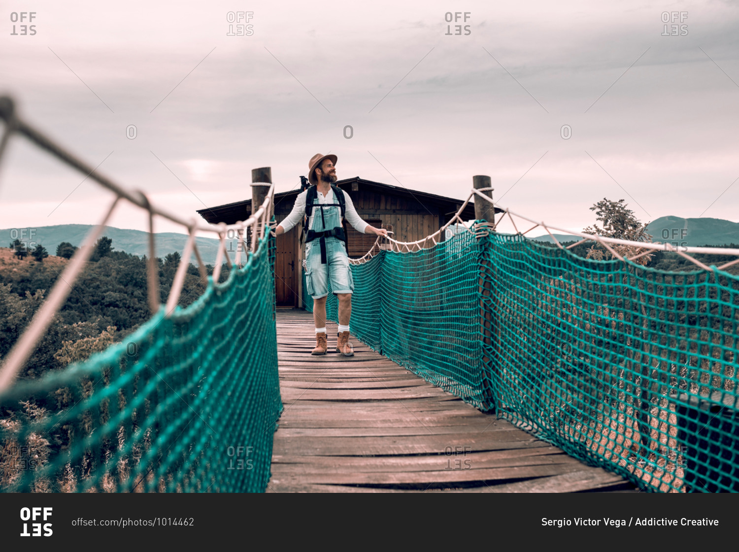 Content male tourist with backpack walking along suspension bridge and admiring amazing landscape during vacation in summer