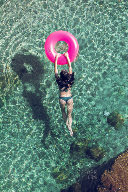 From above female in swimwear swimming in transparent water with inflatable tube on sunny day on resort