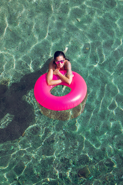From above female in swimwear and sunglasses swimming in transparent water with inflatable tube on sunny day on resort