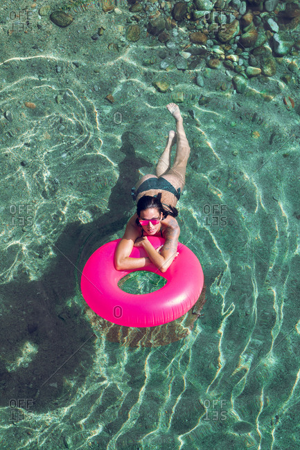 From above female in swimwear and sunglasses swimming in transparent water with inflatable tube on sunny day on resort