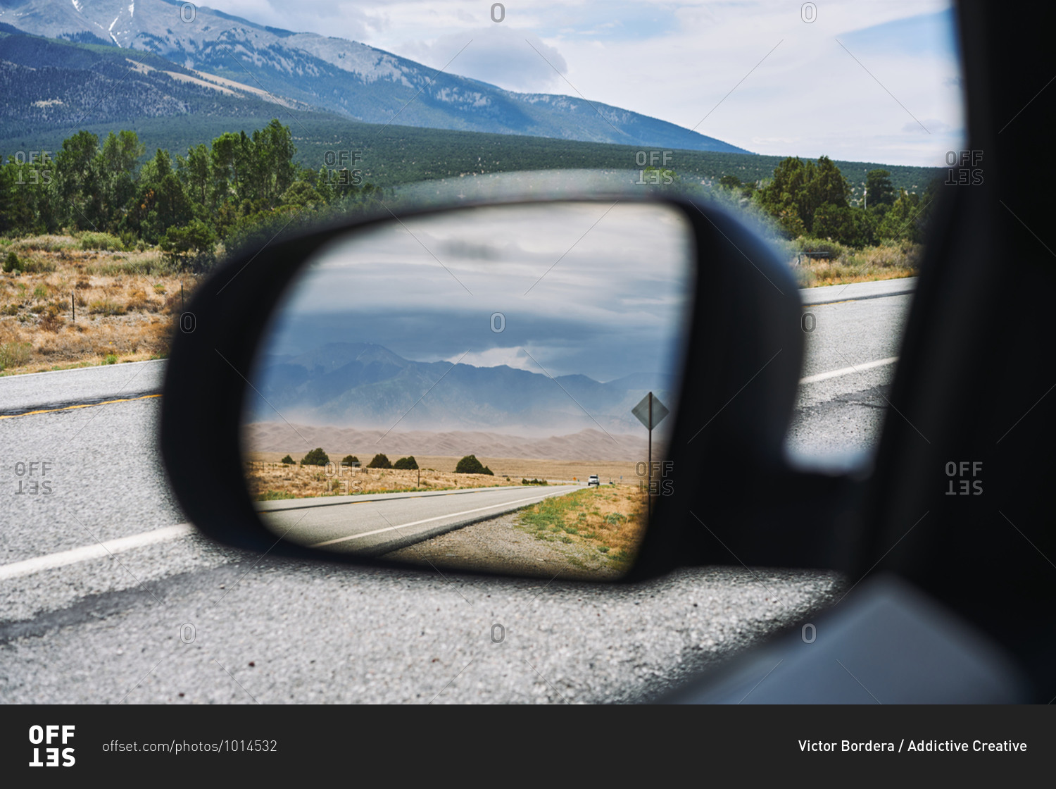 Automobile driving along asphalt road on background of mountains and reflecting in side view mirror