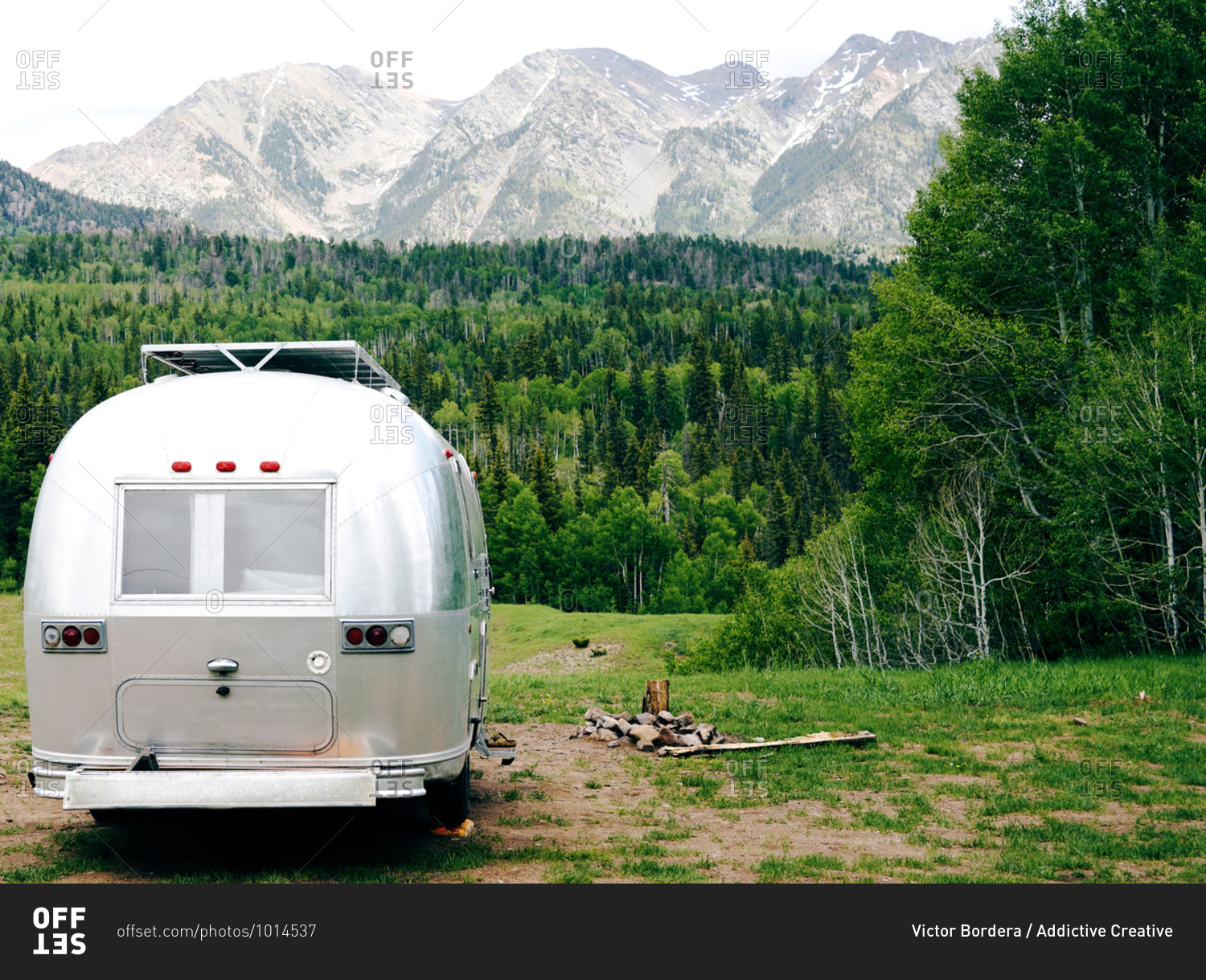 Travel trailer parked on green lawn on background of amazing landscape of mountain range and forest in USA