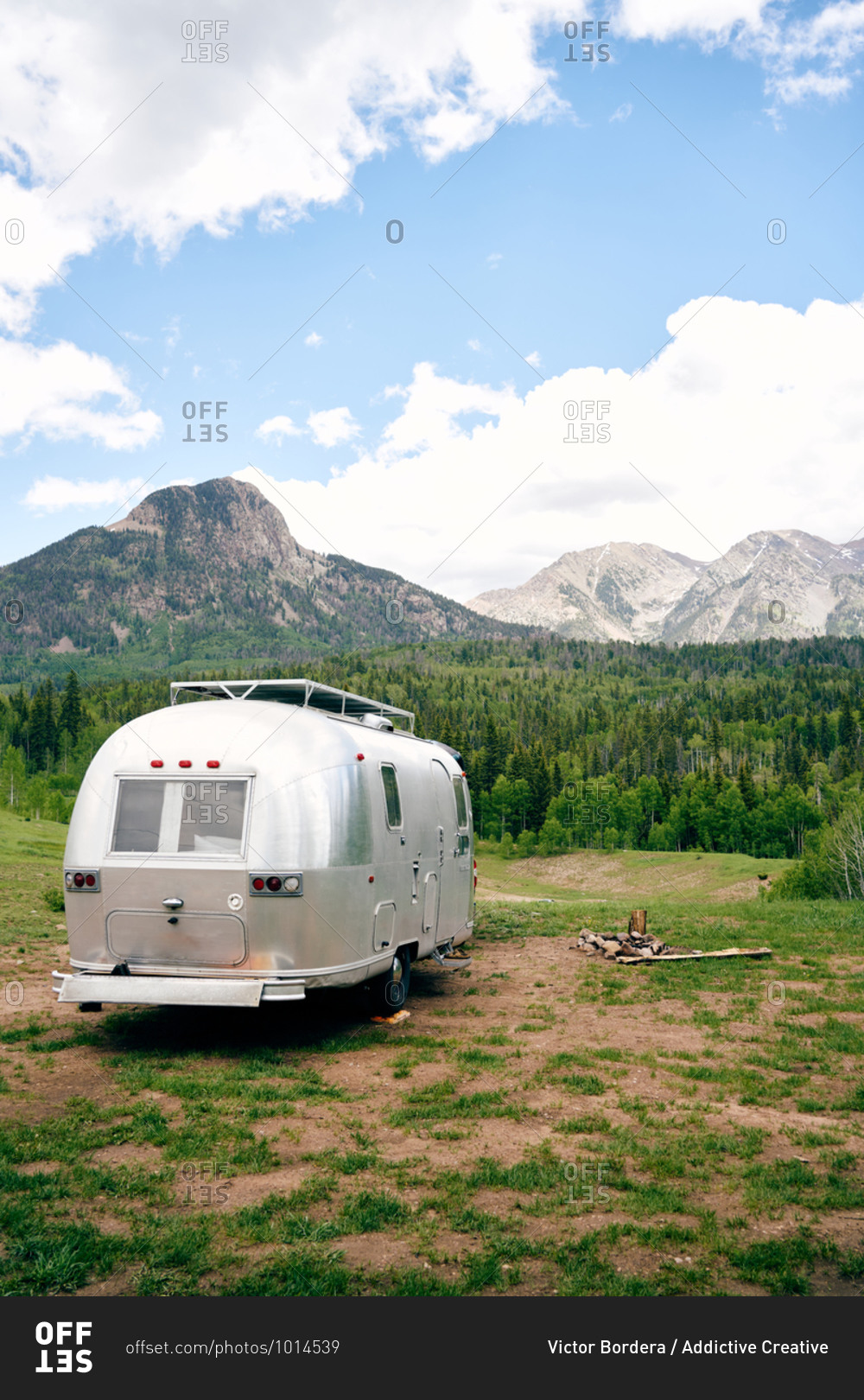 Travel trailer parked on green lawn on background of amazing landscape of mountain range and forest in USA