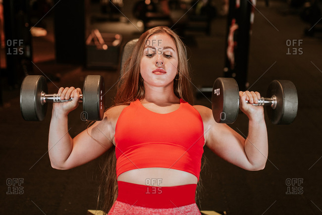 From above strong young sportswoman in bright red sportswear doing dumbbell chest press during functional training in modern gym