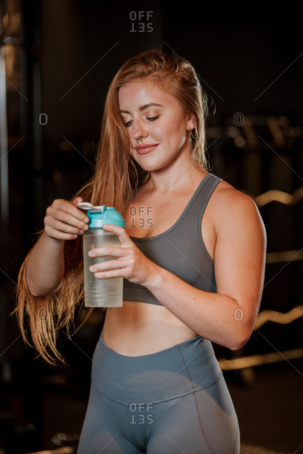 Young fit female in sportswear drinking water from plastic jar while resting after training in gym