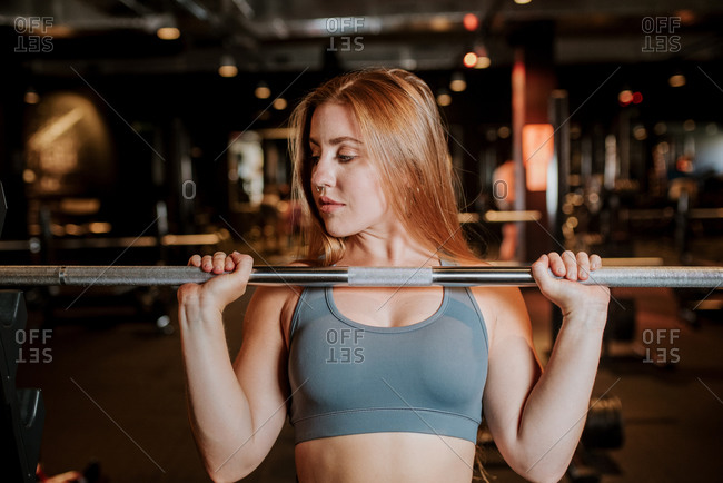 Determined active female in sportswear doing overhead press barbell while exercising with weight in contemporary gym