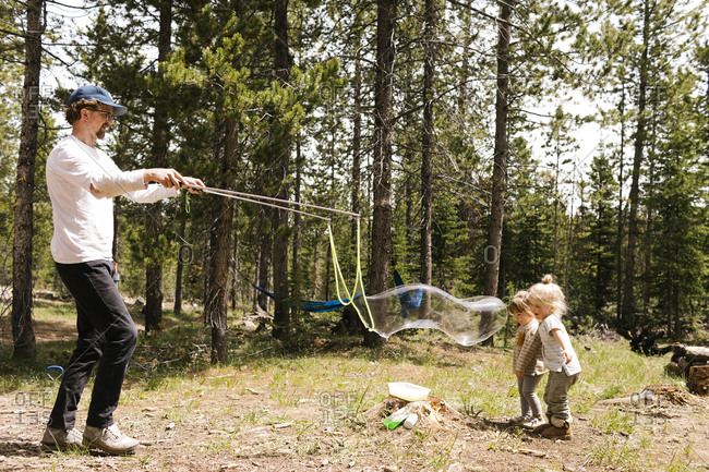 Father making large soap bubbles in forest for two daughters (2-3, 4-5), Wasatch-Cache National Forest