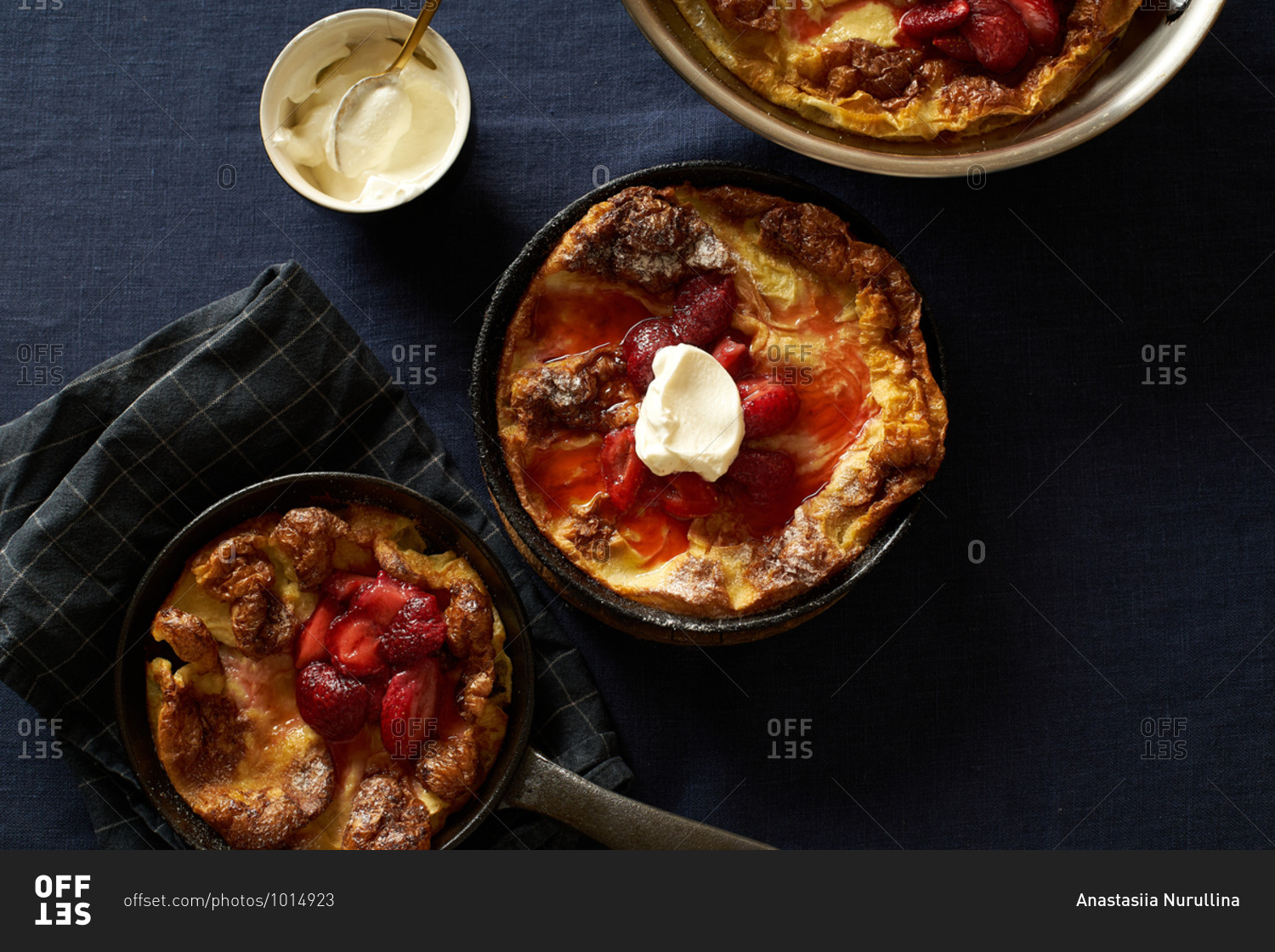 Dutch baby pancakes in various pans with poached strawberries and cream