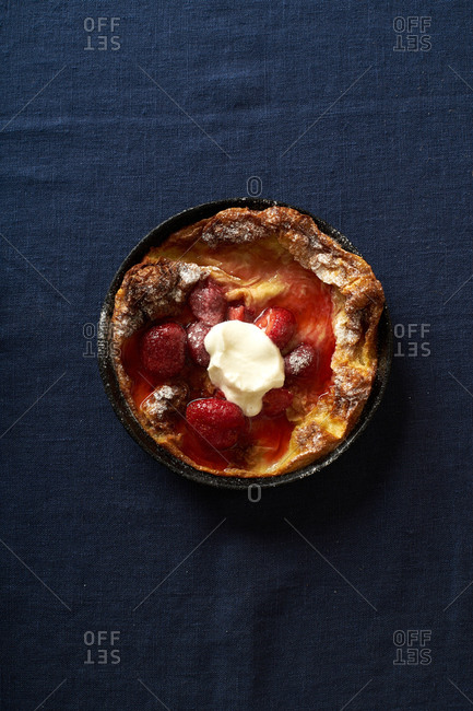 Top view of dutch baby pancake in a pan with poached strawberries and cream