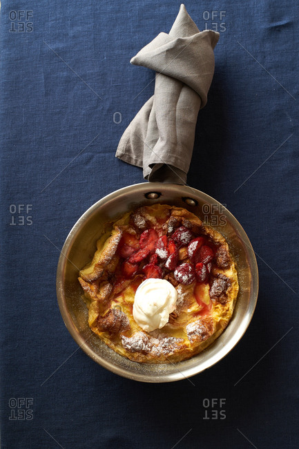 Top view of dutch baby pancake in a pan with poached strawberries and cream
