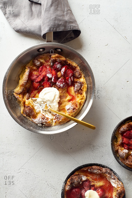 Dutch baby pancakes in various pans with poached strawberries and cream