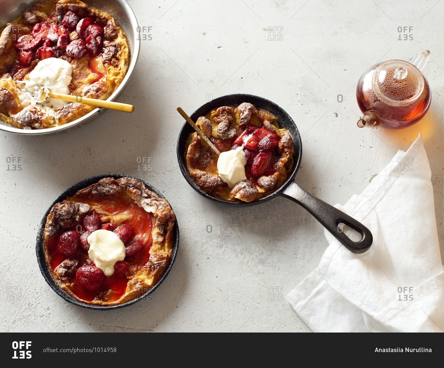 Overhead image of dutch baby pancakes in three different pans with poached strawberries and cream
