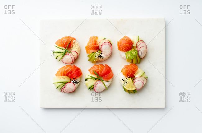 Sushi donuts with salmon and crunchy vegetables on marble cutting board. Top view with copy space.