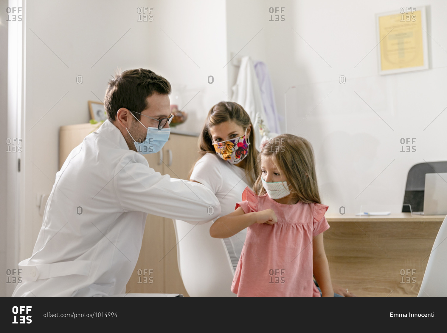 Medical practitioner and little patient in masks greeting each other with elbow bump