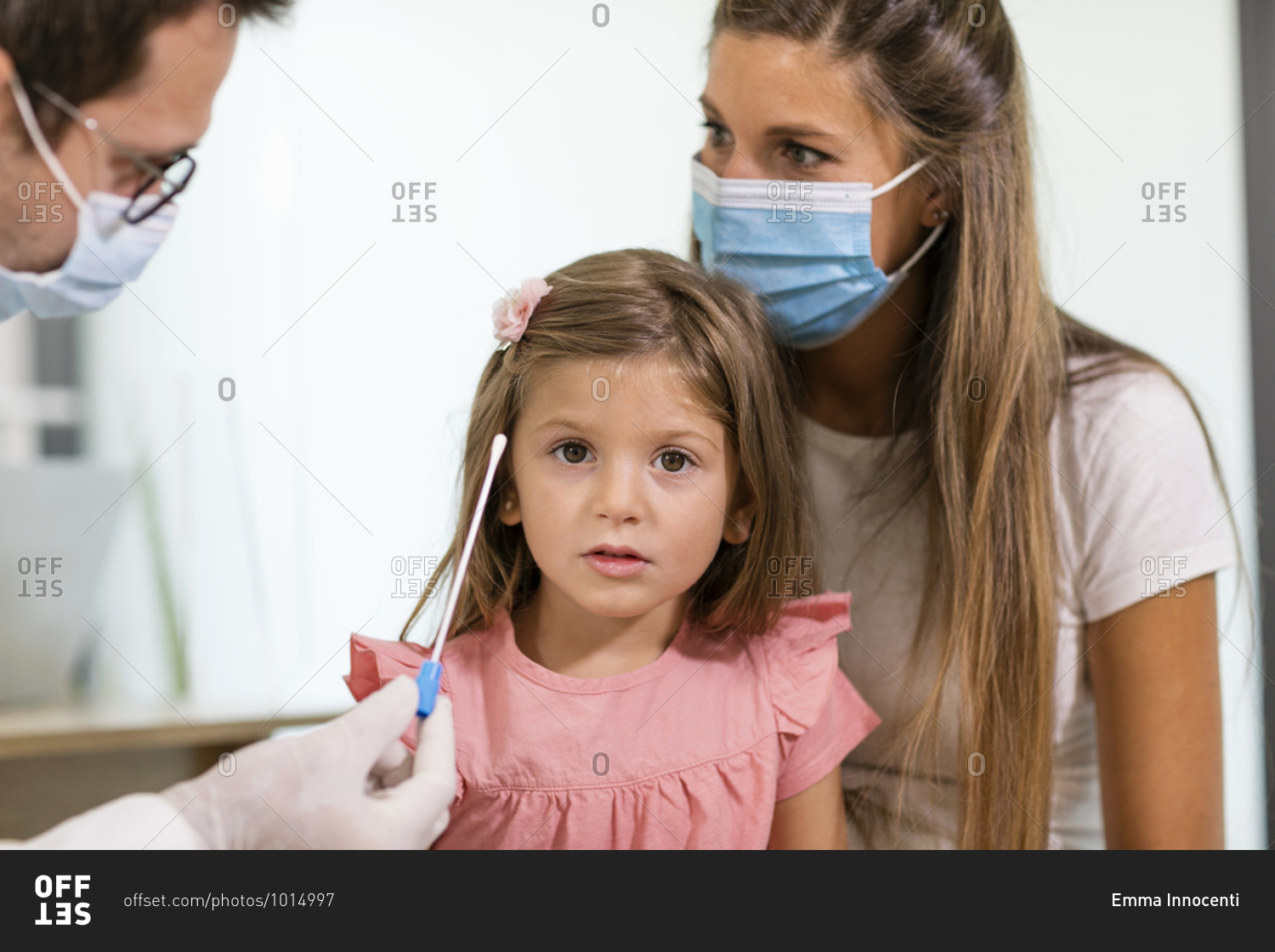 Medical practitioner in gloves and mask demonstrating test swab to mother and daughter during appointment in clinic