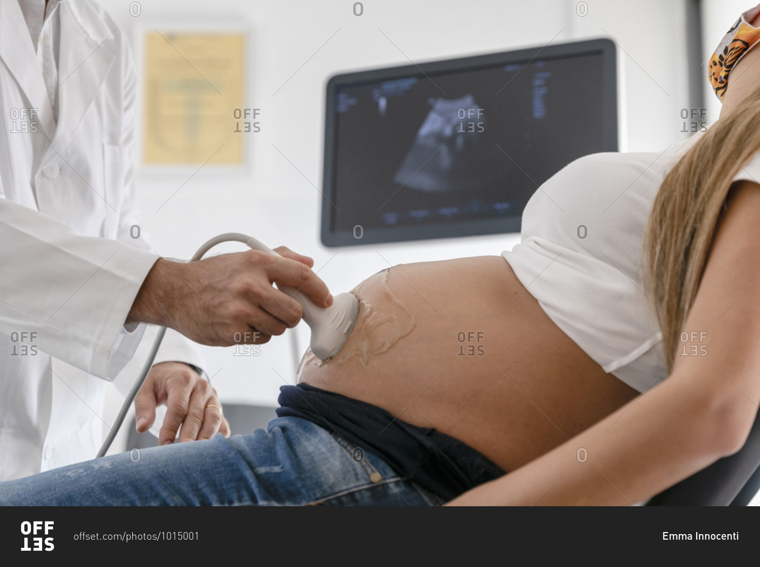 Unrecognizable medical practitioner using modern equipment to do sonography on pregnant female in mask