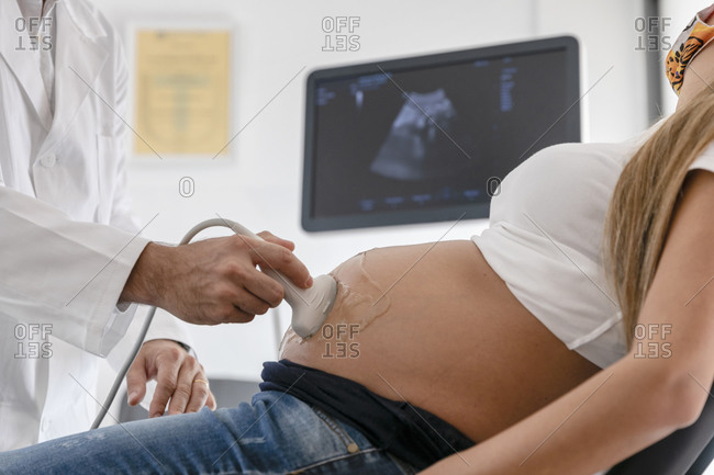Unrecognizable medical practitioner using modern equipment to do sonography on pregnant female in mask