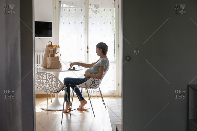 Young expecting mother touching tummy and enjoying delicious fresh fruits in home kitchen