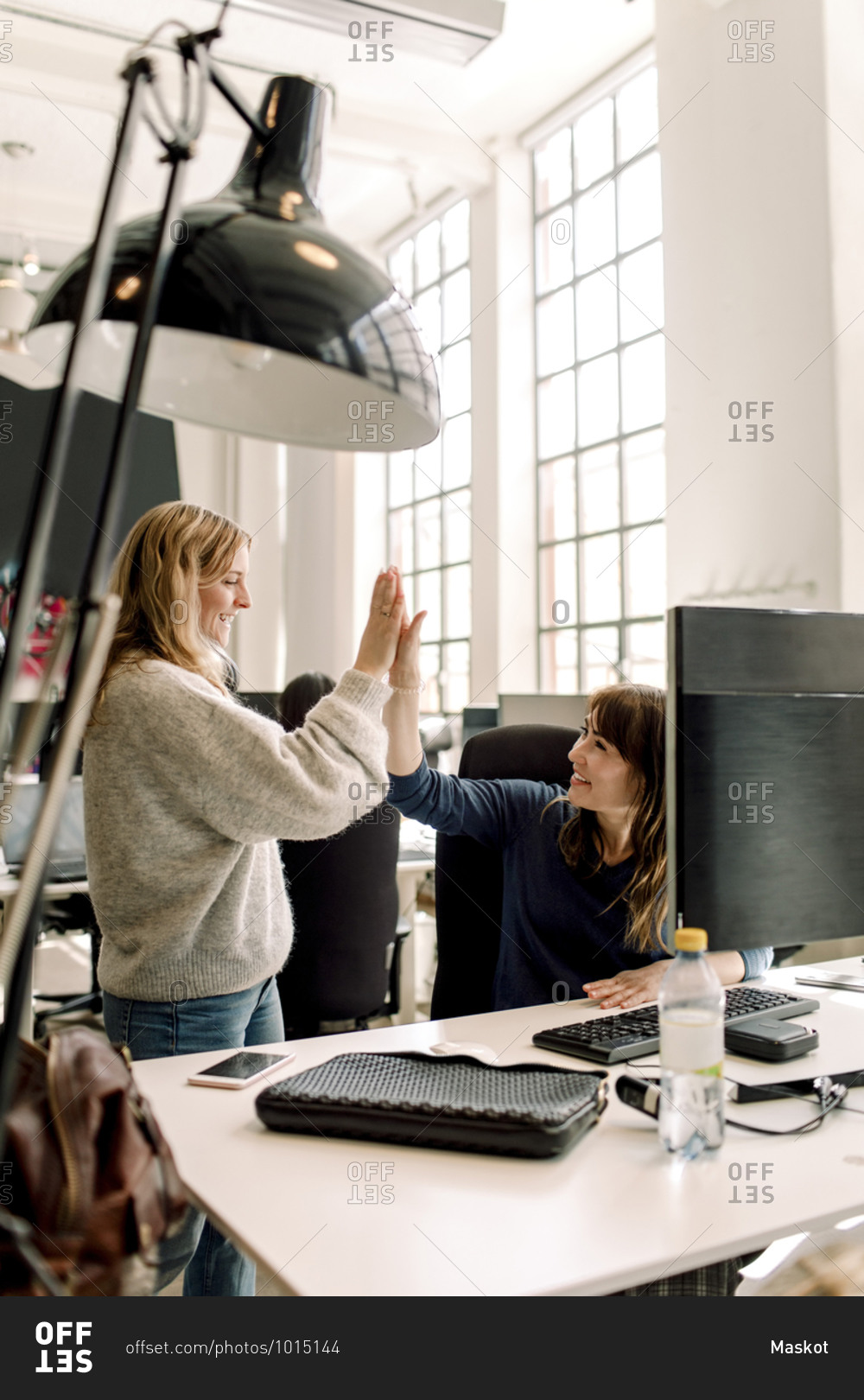 Smiling female colleagues giving high-five at workplace