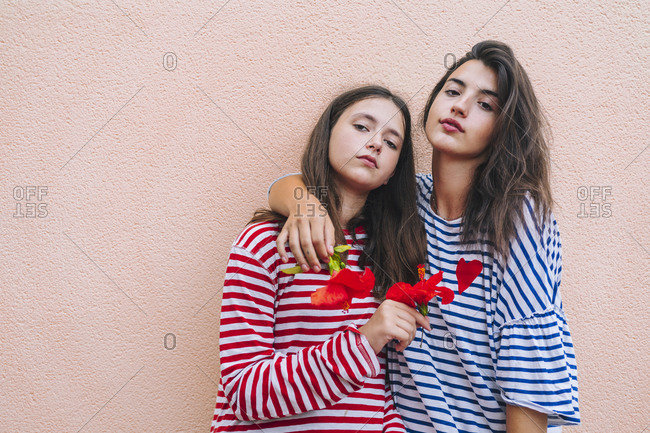 Sisters holding hibiscus flowers while standing against wall