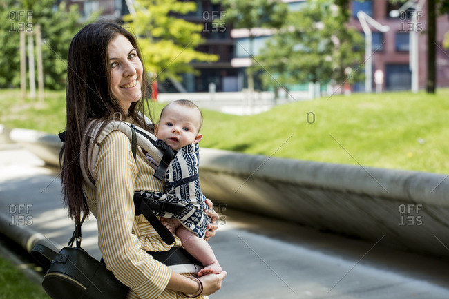 Smiling mother with her baby boy in baby carrier in city
