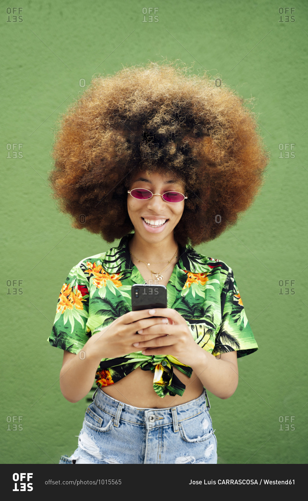 Smiling young woman using smartphone in front of green wall