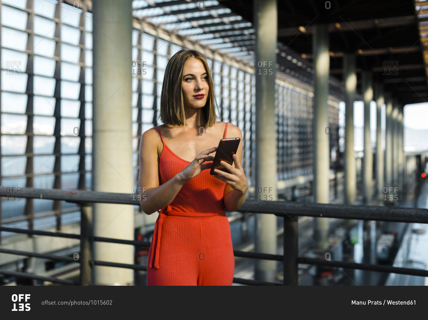Beautiful young woman looking away while holding smart phone at railroad station