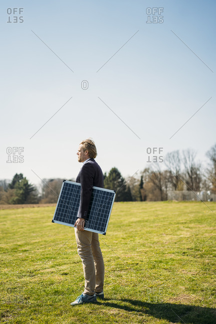 Male entrepreneur holding solar panel while looking away at park on sunny day