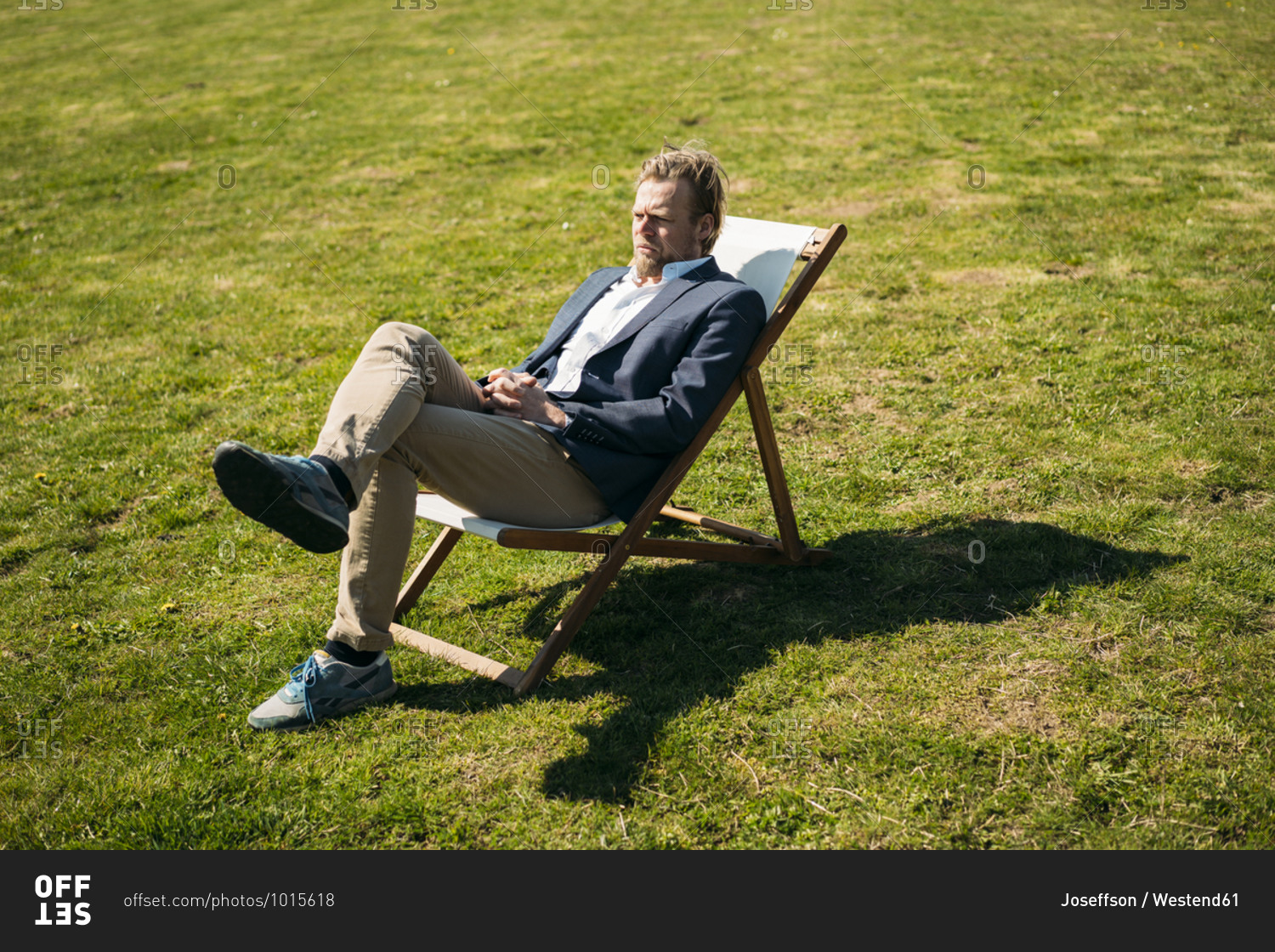 Relaxed businessman sitting on chair while looking away at park during sunny day