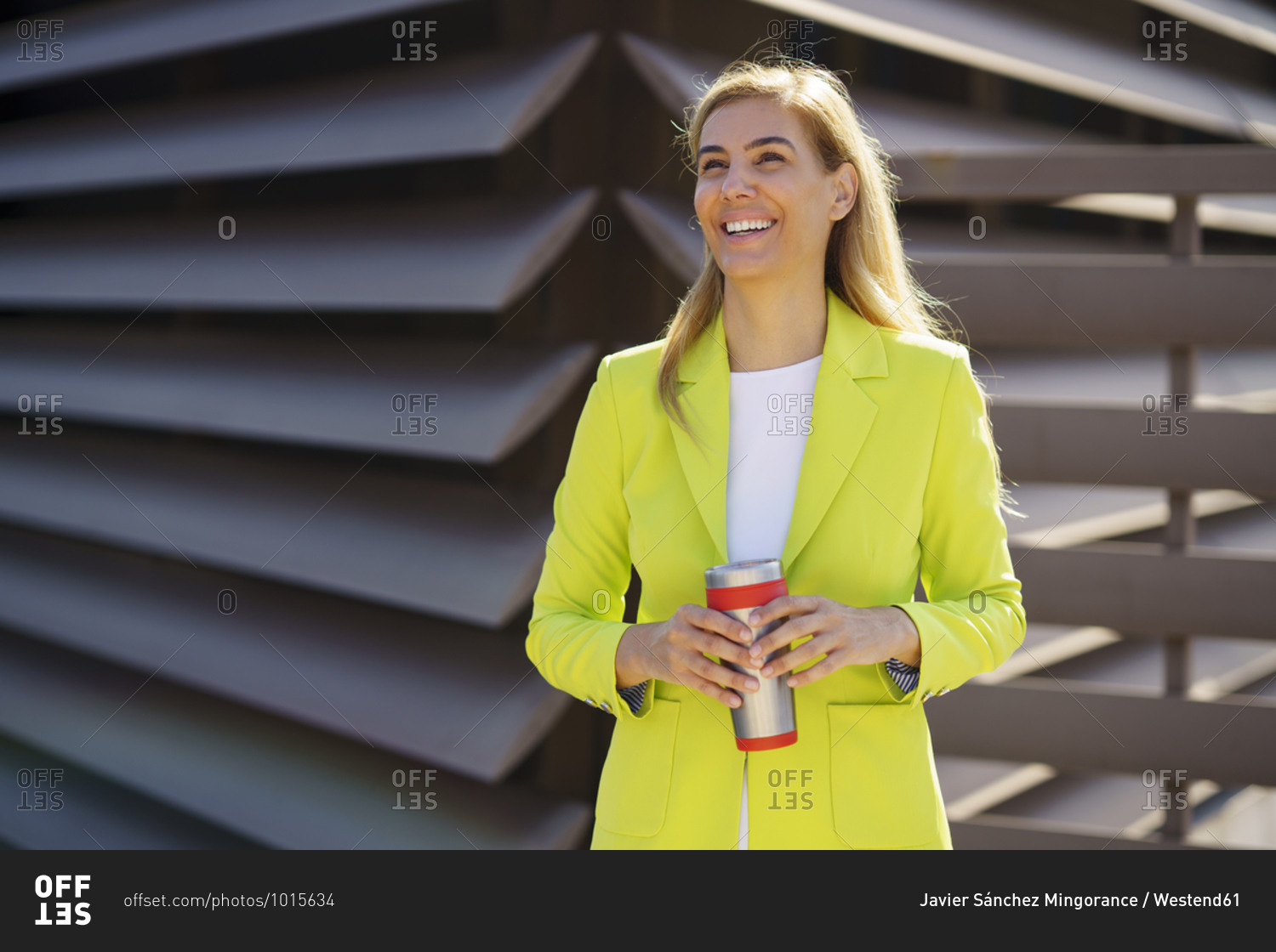 Smiling businesswoman with travel mug looking away while standing against railing