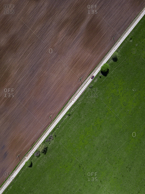Aerial view of car driving along countryside road stretching between green and brown field