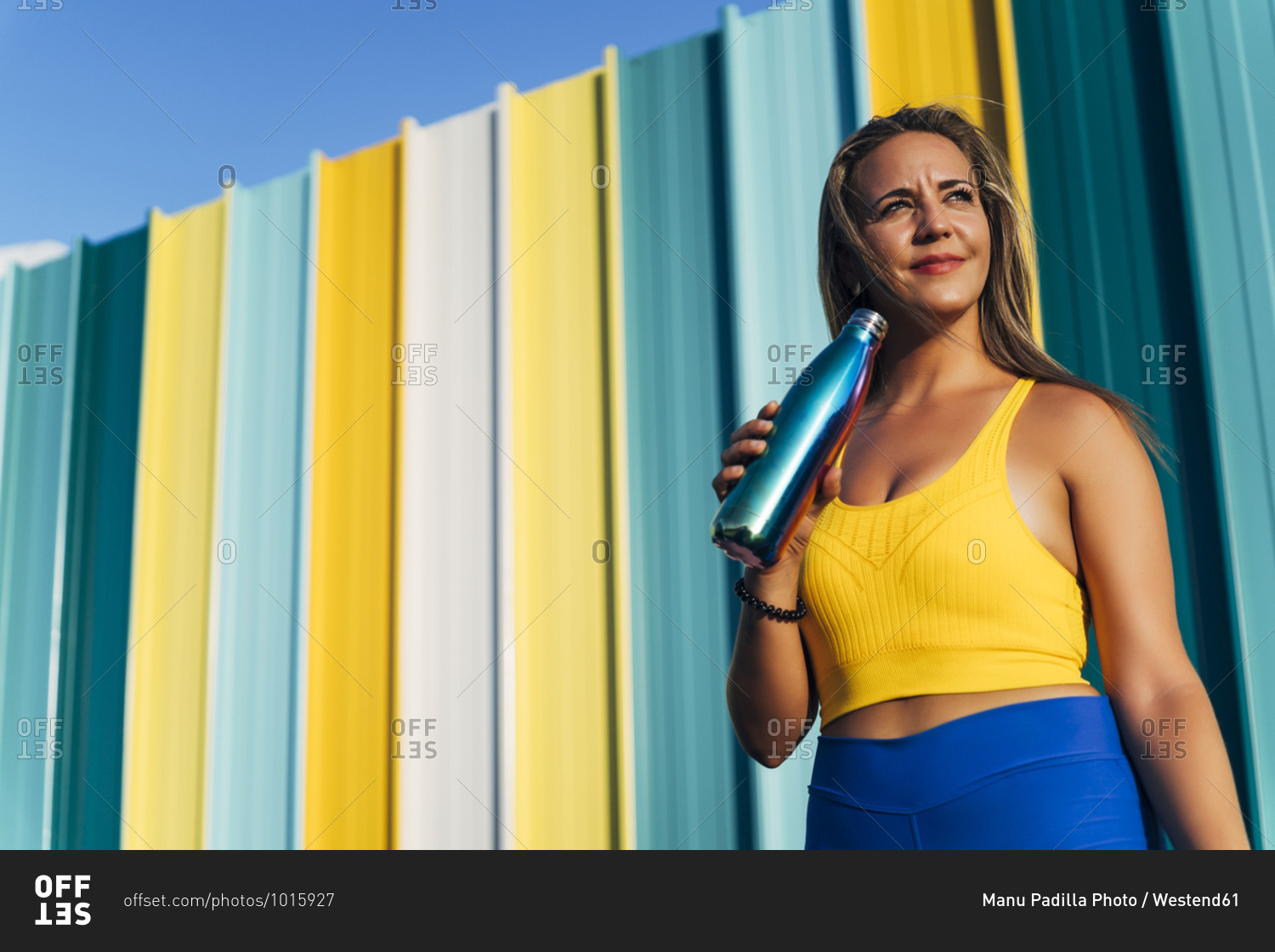 Female jogger with vacuum flask in front of colorful wall