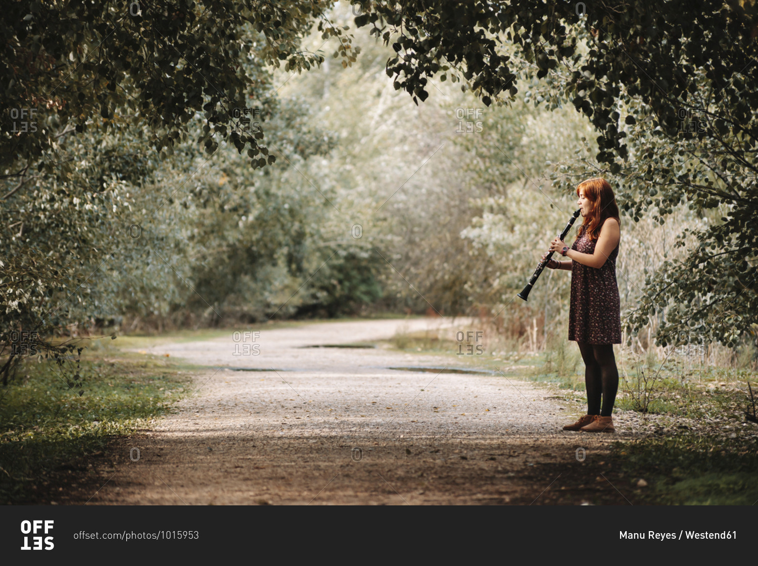 Young woman practicing clarinet while standing on footpath in forest
