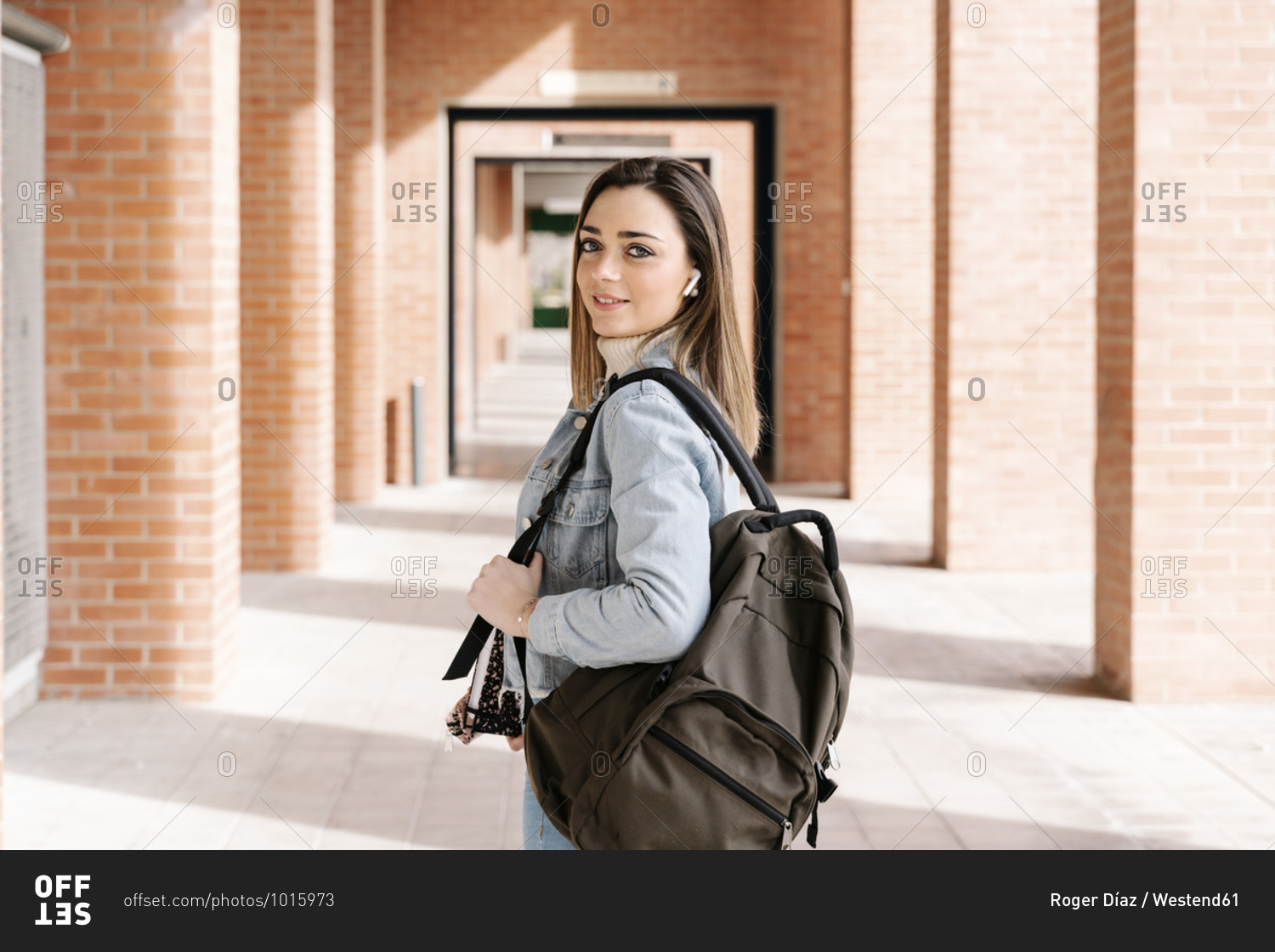 Smiling university student with bag and book standing in campus