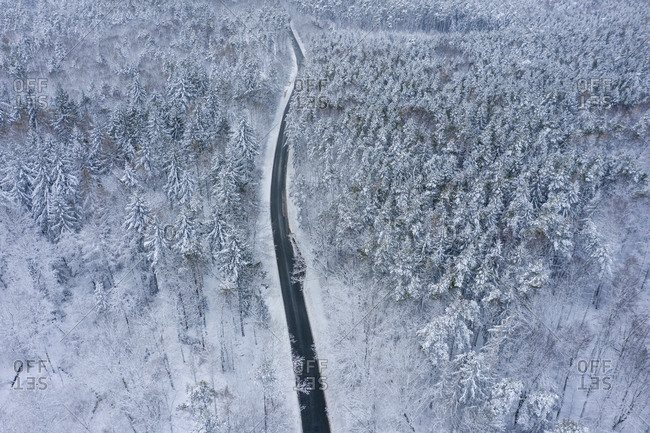 Drone view of asphalt road cutting through snow-covered forest in Franconian Heights