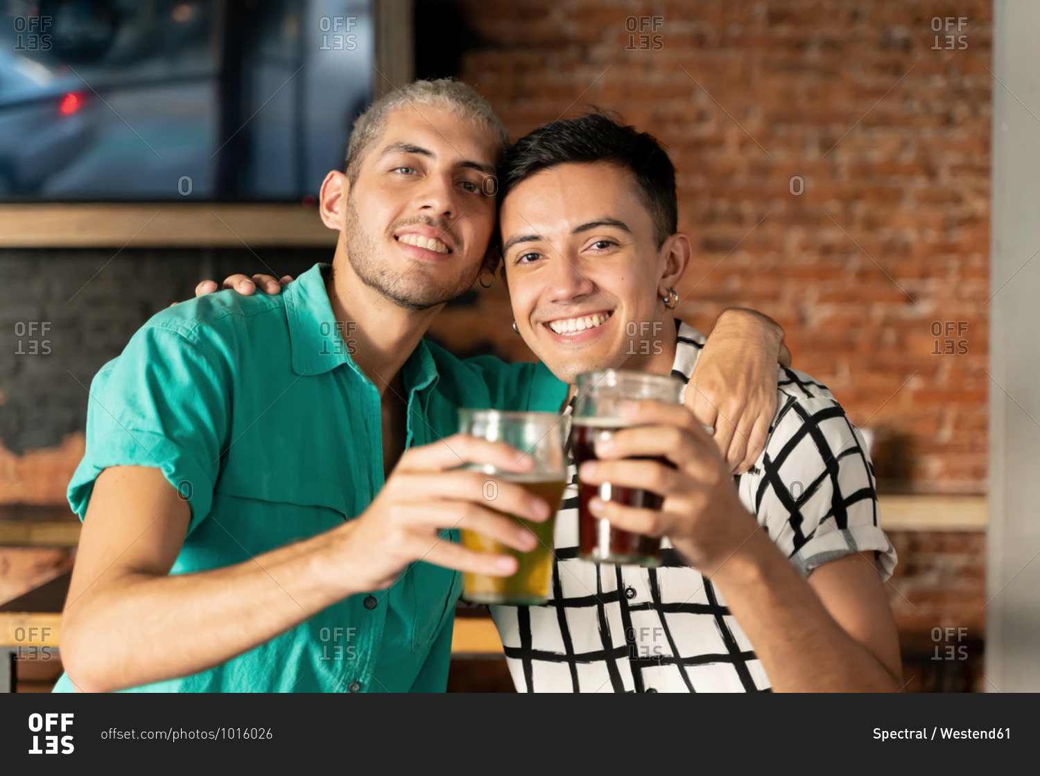 Happy gay couple with arm around holding beer glass at bar