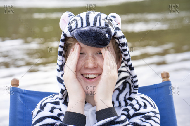 Smiling boy in zebra costume sitting on chair against lake