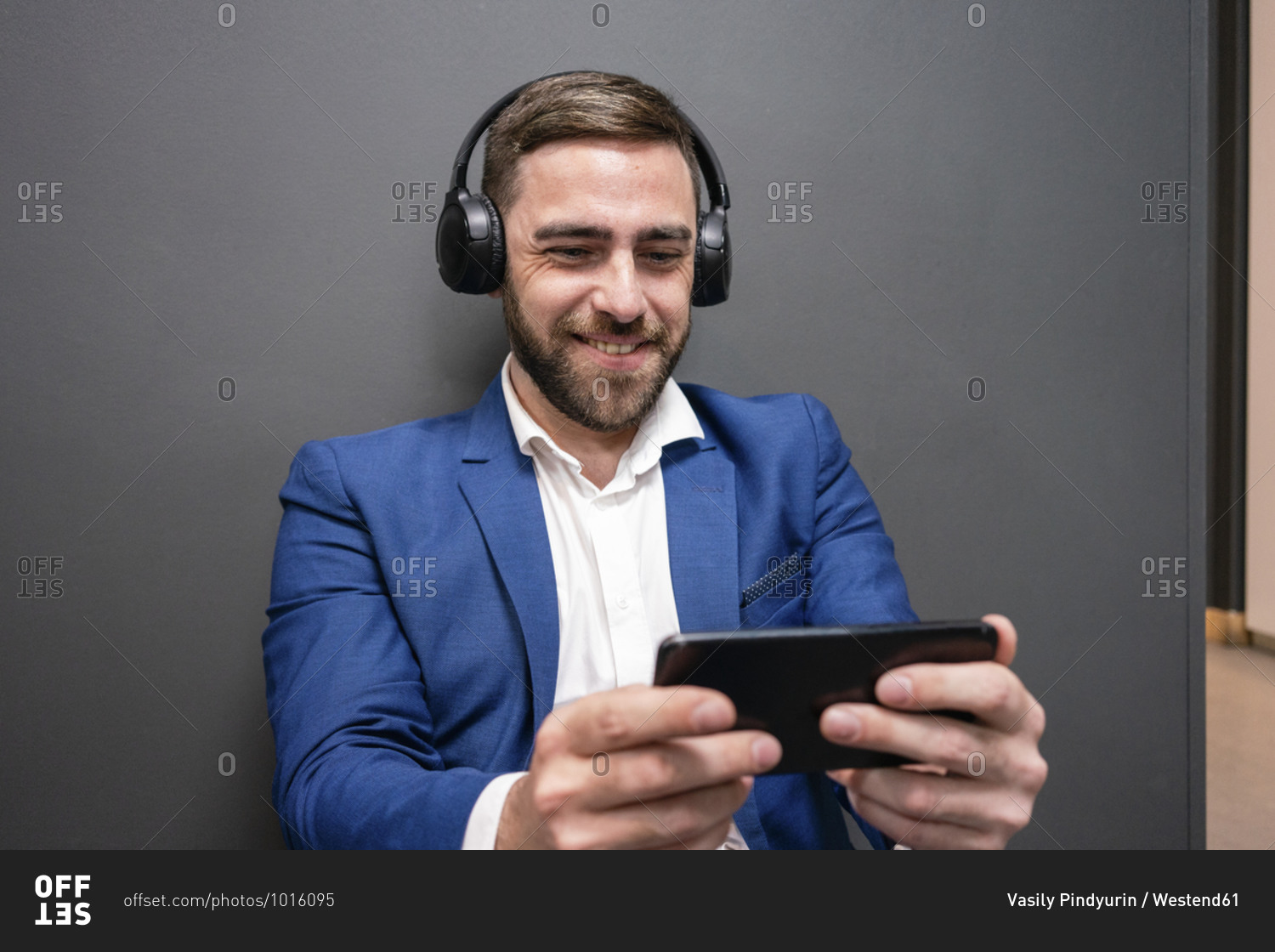 Smiling businessman playing video game on smart phone while sitting in corridor at creative office during break
