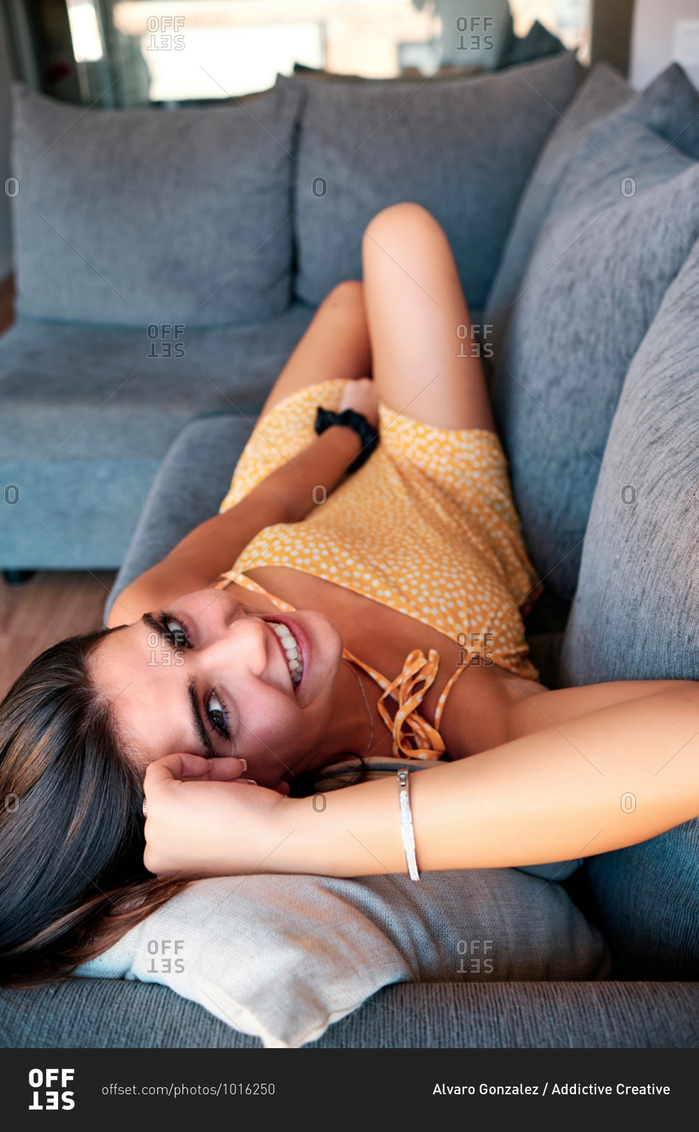 From above of happy female in dress relaxing on couch in living room looking at camera
