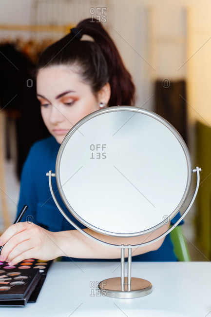 Young beautiful female makeup artist sitting at table with eyeshadow palette applying makeup with brush