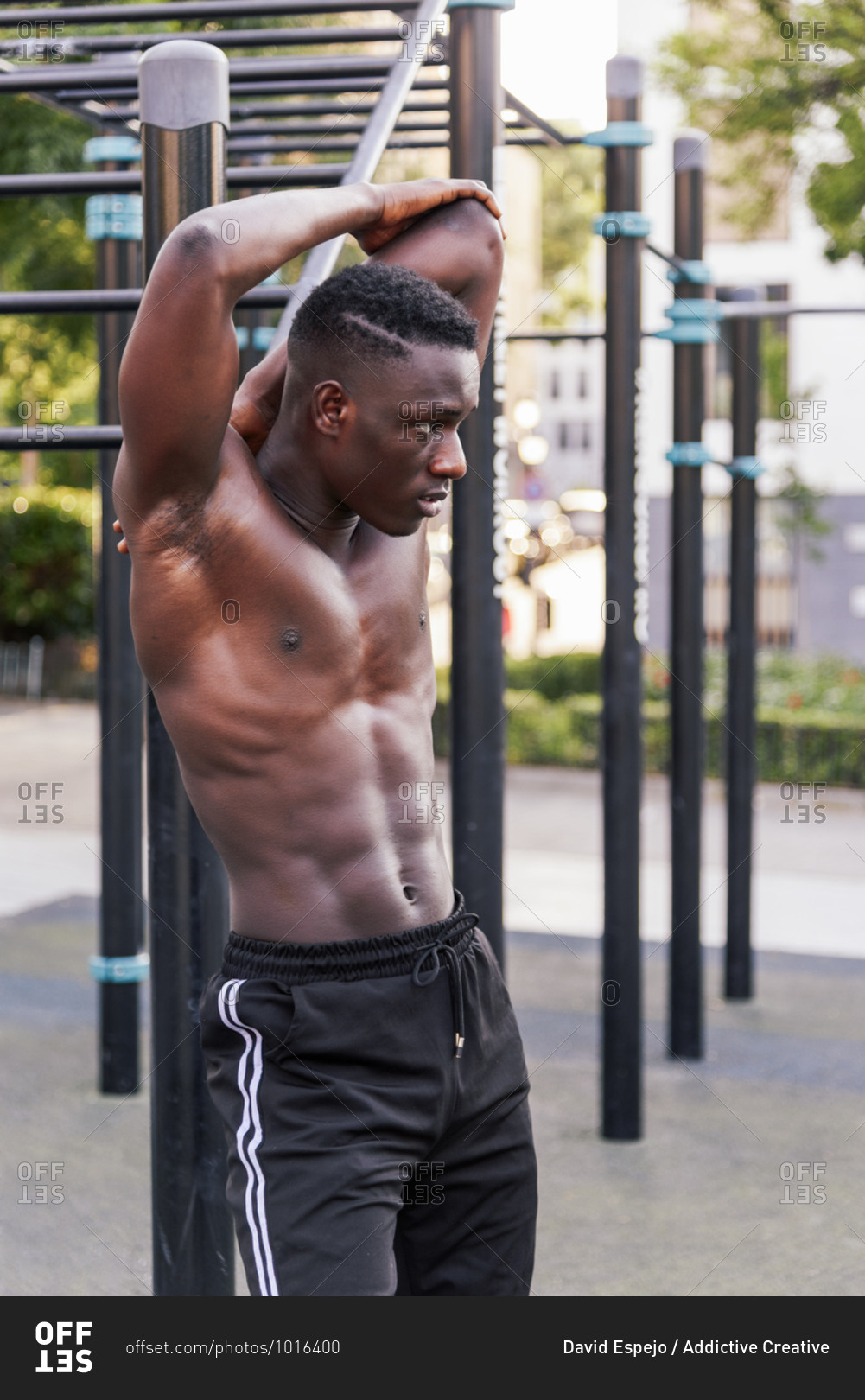 African American male athlete with naked torso standing on sports ground and stretching arms behind back before training and looking away