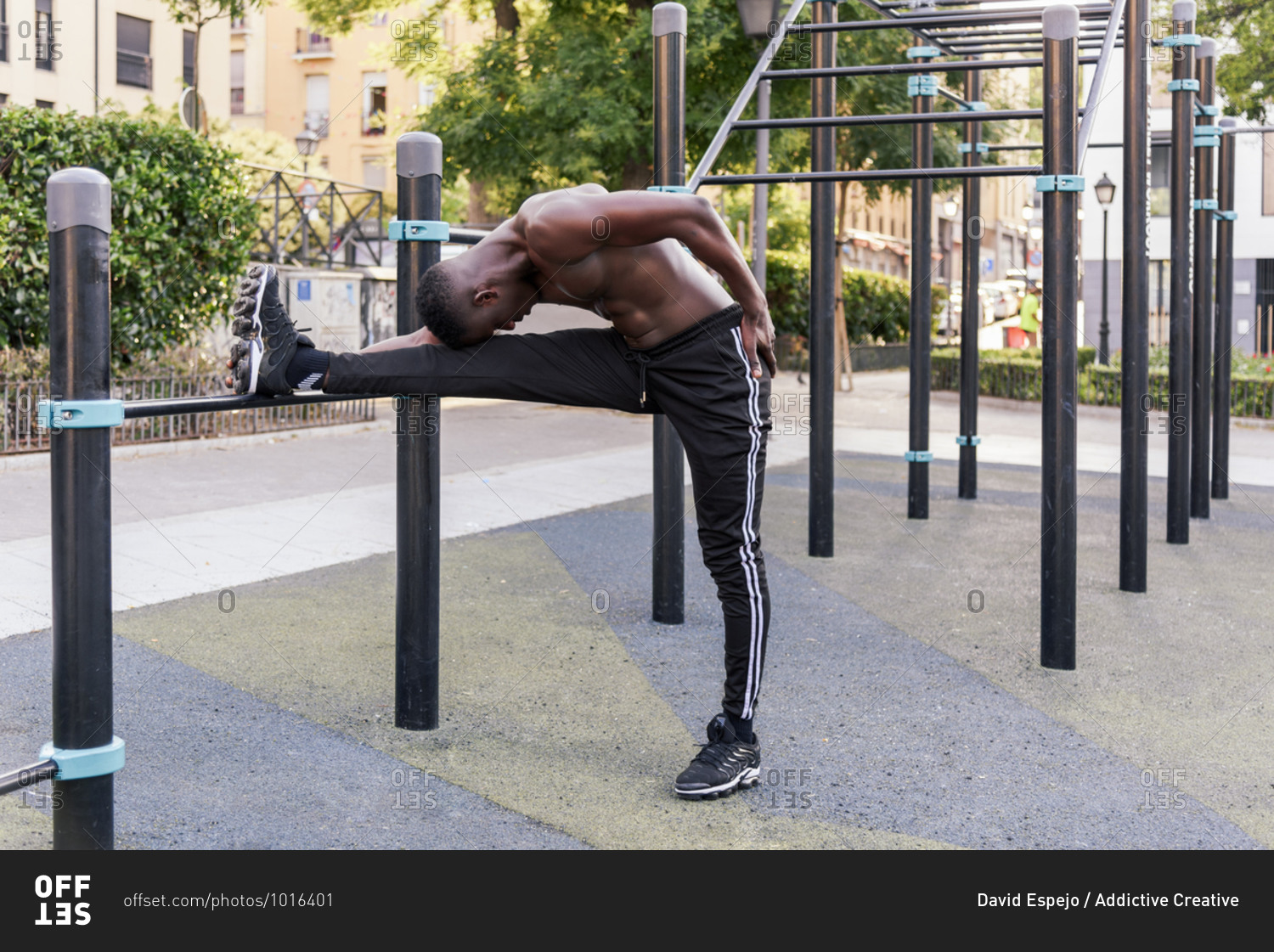 Side view of flexible African American athletic male standing on sports ground and stretching legs while doing forward bend during workout