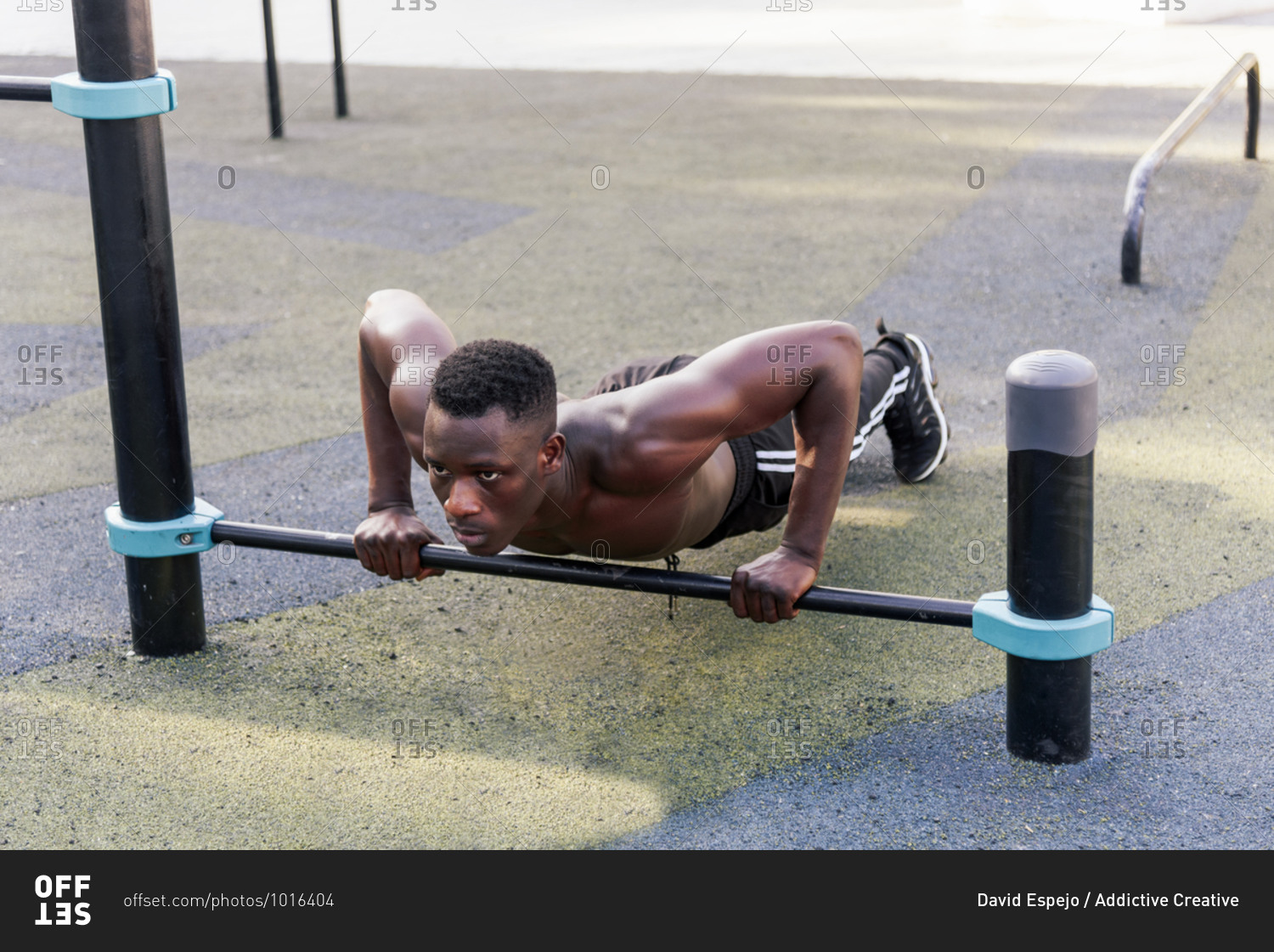 Concentrated black sportsman doing push ups wit metal crossbar during active workout and looking forward