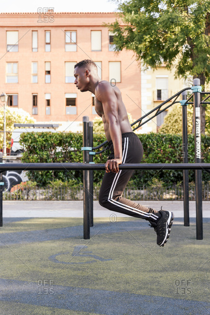 Focused African American male athlete doing pull ups on crossbar during intense training on sports ground in city