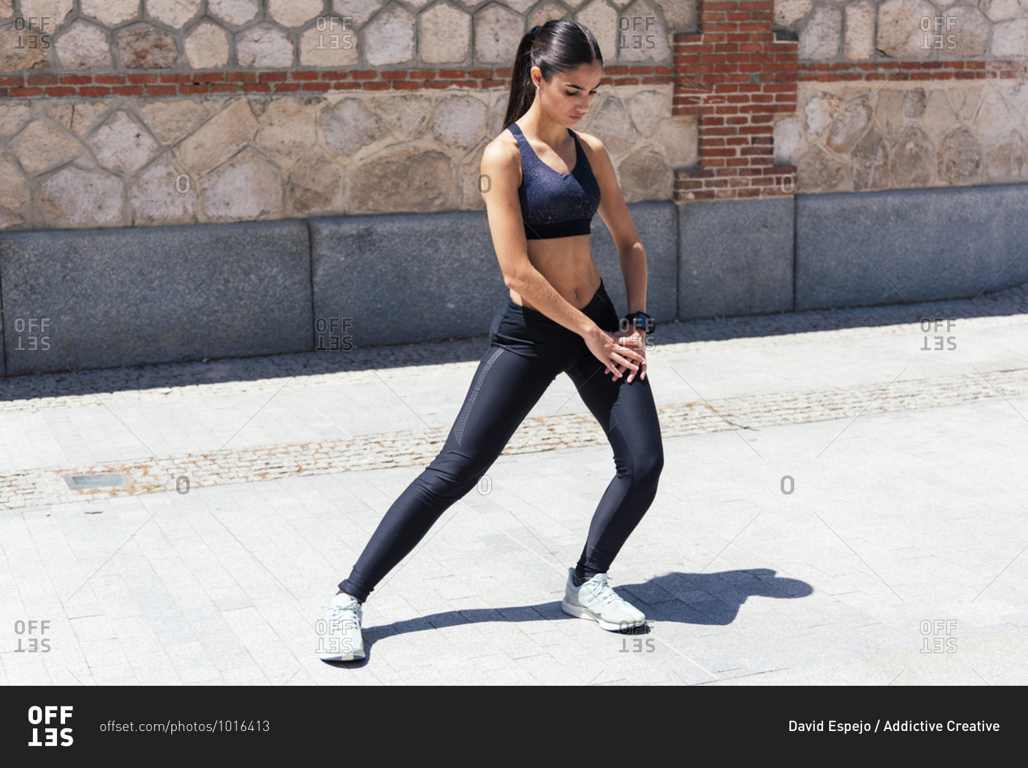 Full body of slim young female athlete in sportswear doing side lunges while stretching legs before running on street