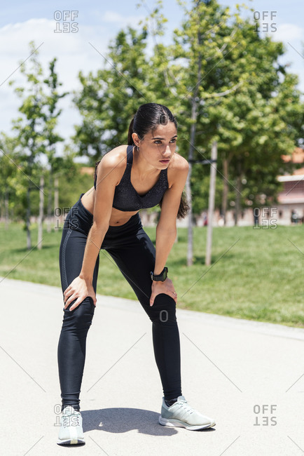 Exhausted fit female runner in activewear standing on pavement and having break during intense training while looking away