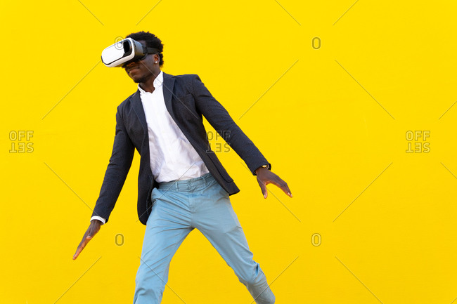 African American male standing experiencing virtual reality while using modern VR headset on yellow background in city