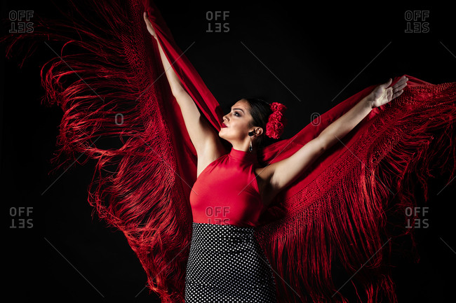 Seductive young Hispanic female in traditional red costume performing sensual Flamenco dance and looking away
