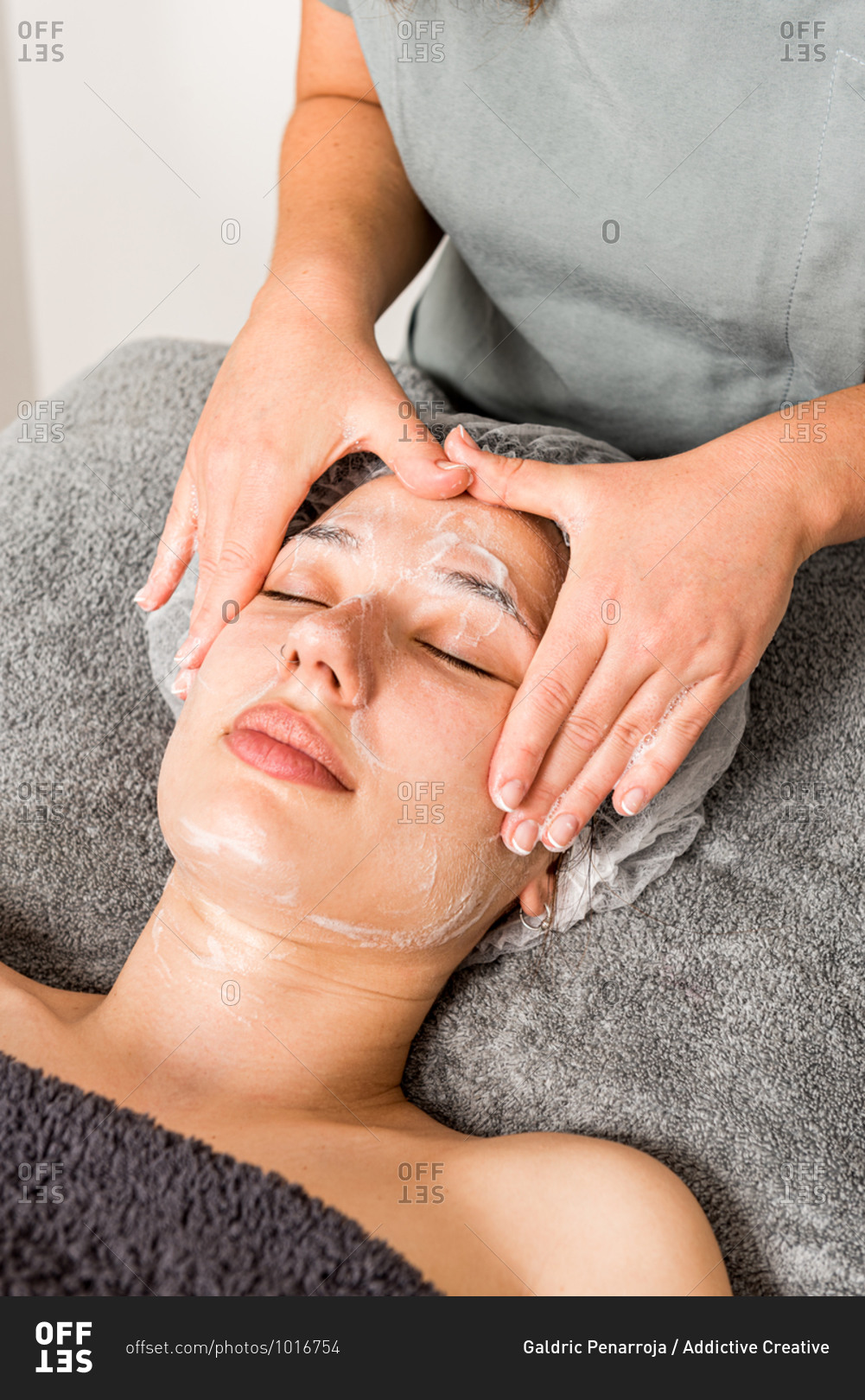 Crop anonymous cosmetician applying facial cloth mask on female client during rejuvenate skincare procedure in modern beauty salon